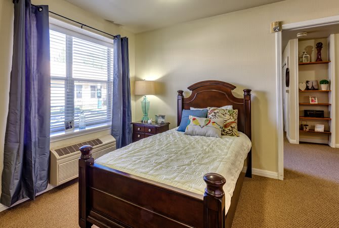 A cozy bedroom with a wooden bed frame, a bedside lamp, and a window letting in natural light.