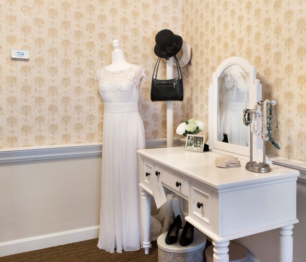 A charming vintage-inspired dressing room with a white dress on display and an elegant vanity table adorned with accessories.