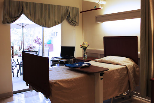 A well-lit hospital patient room featuring a bed, desk, and window.