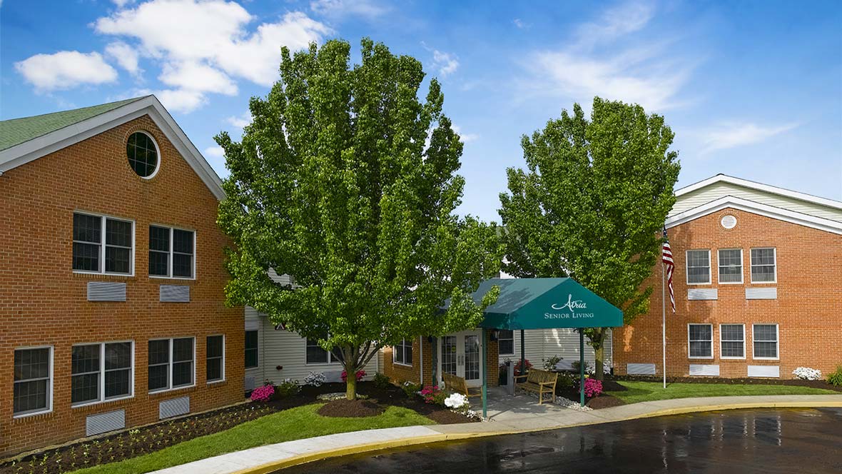 A building entrance with a green awning, surrounded by lush trees and landscaping.