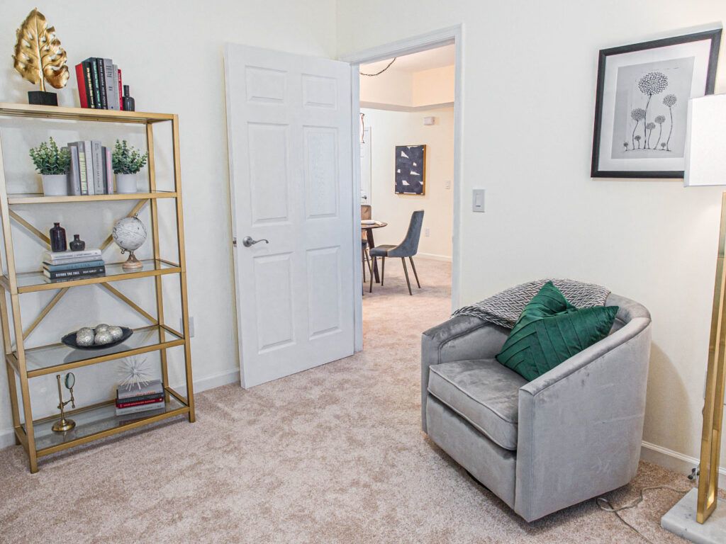 Cozy living room with an armchair and bookshelf leading into a dining area.