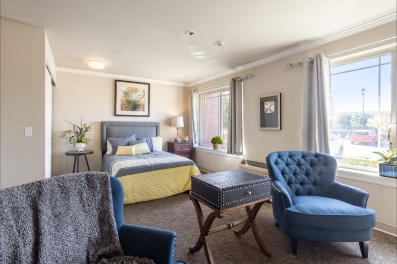 A cozy bedroom with elegant furnishings, featuring a bed, armchairs, and warm lighting.