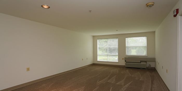An empty room with carpet flooring and large windows allowing natural light.