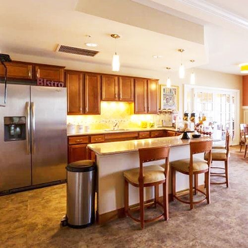 A modern kitchen with wooden cabinets and stainless steel appliances, featuring an island counter with chairs and stylish lighting.