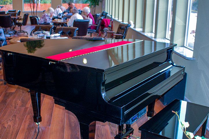 A grand piano in a restaurant setting with diners in the background.