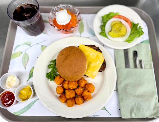 A meal served on a tray featuring a burger, sweet potato tots, salad, and a dessert.