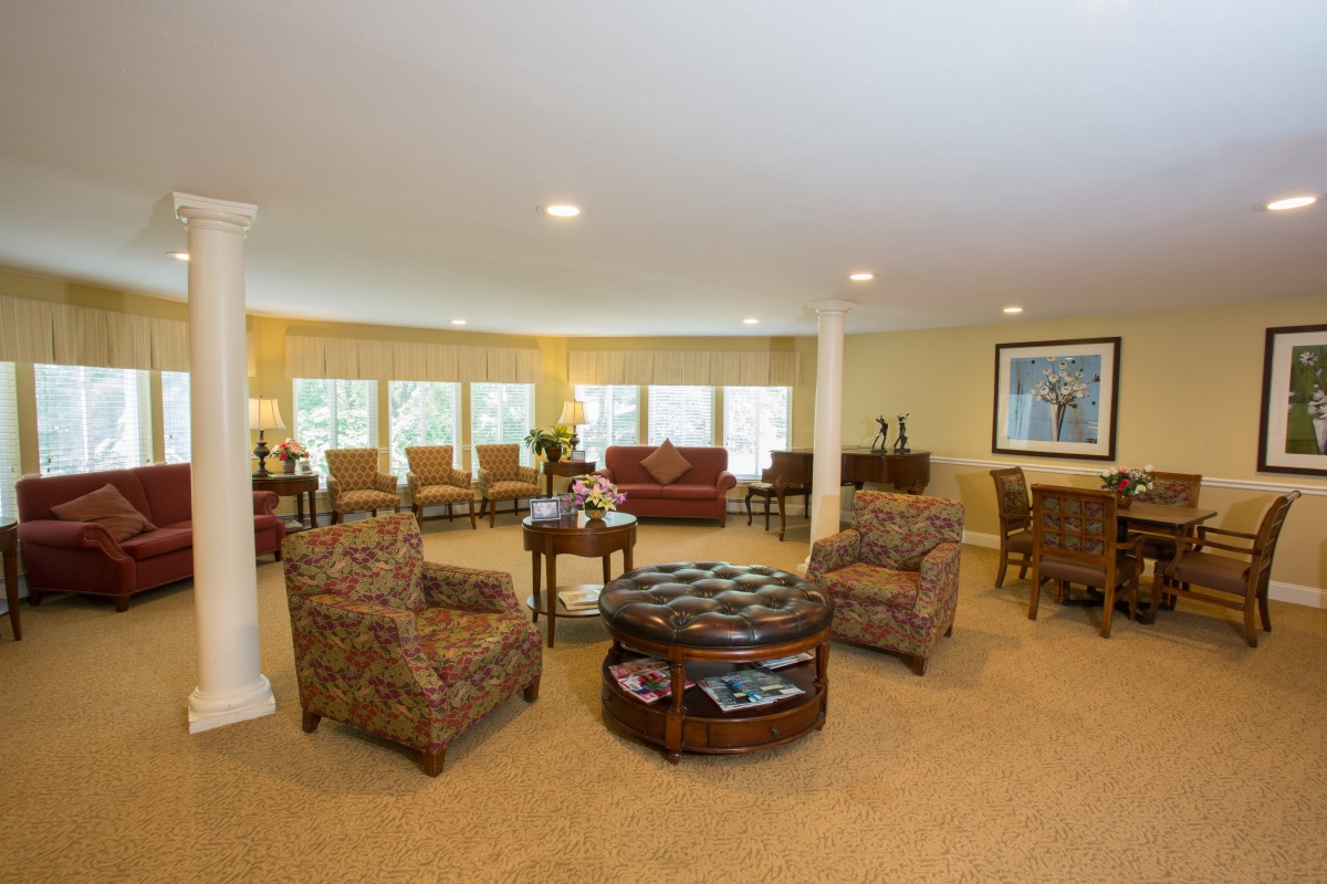 A spacious living room featuring cozy armchairs and a central coffee table, surrounded by large windows.