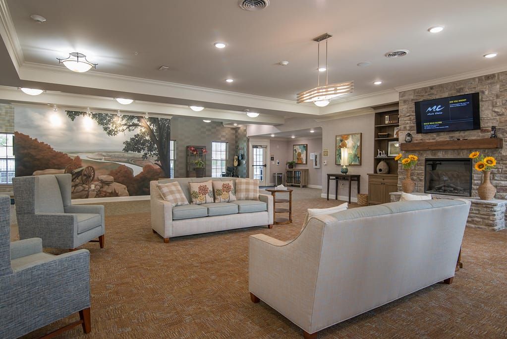A spacious and elegantly decorated lounge area featuring white sofas, chandeliers, and artwork on the walls.