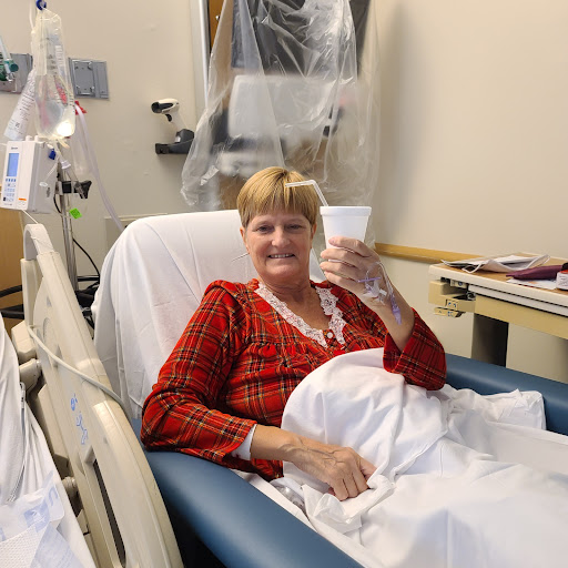 A smiling patient holding a cup while resting in a hospital bed.