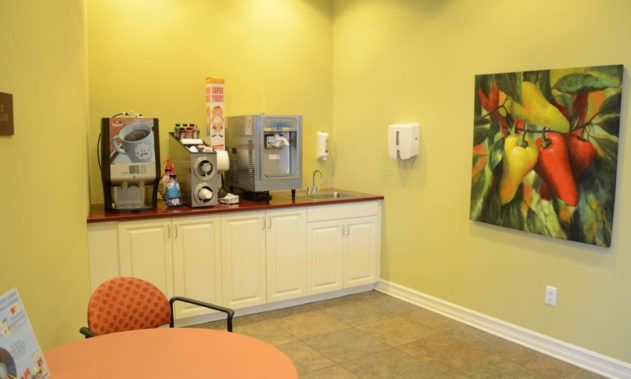 A waiting room with a beverage station, featuring a coffee machine and seating.