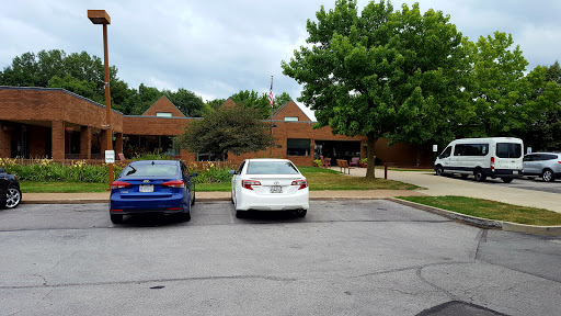 A view of a parking lot with two cars parked in front of a building surrounded by greenery.