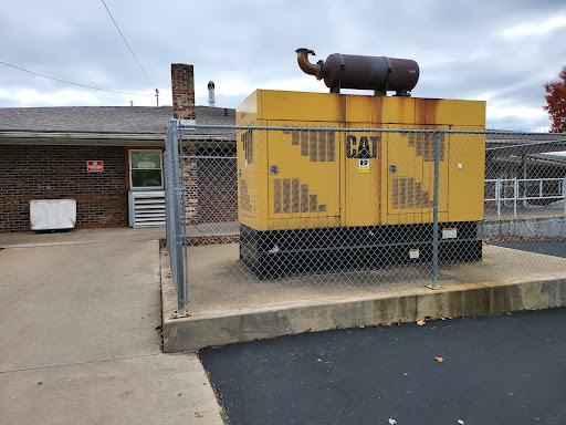 A yellow industrial generator secured behind a fence next to a building.
