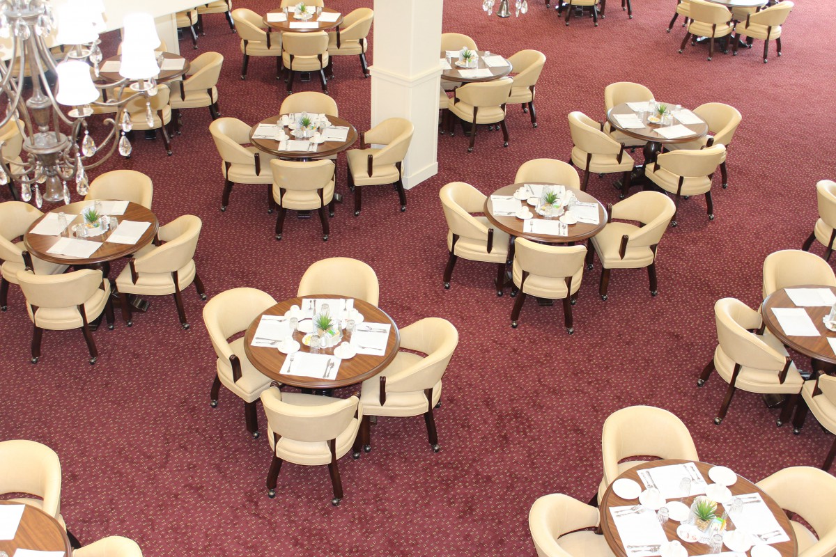 An elegantly arranged dining area with round tables and comfortable chairs on a red carpet.