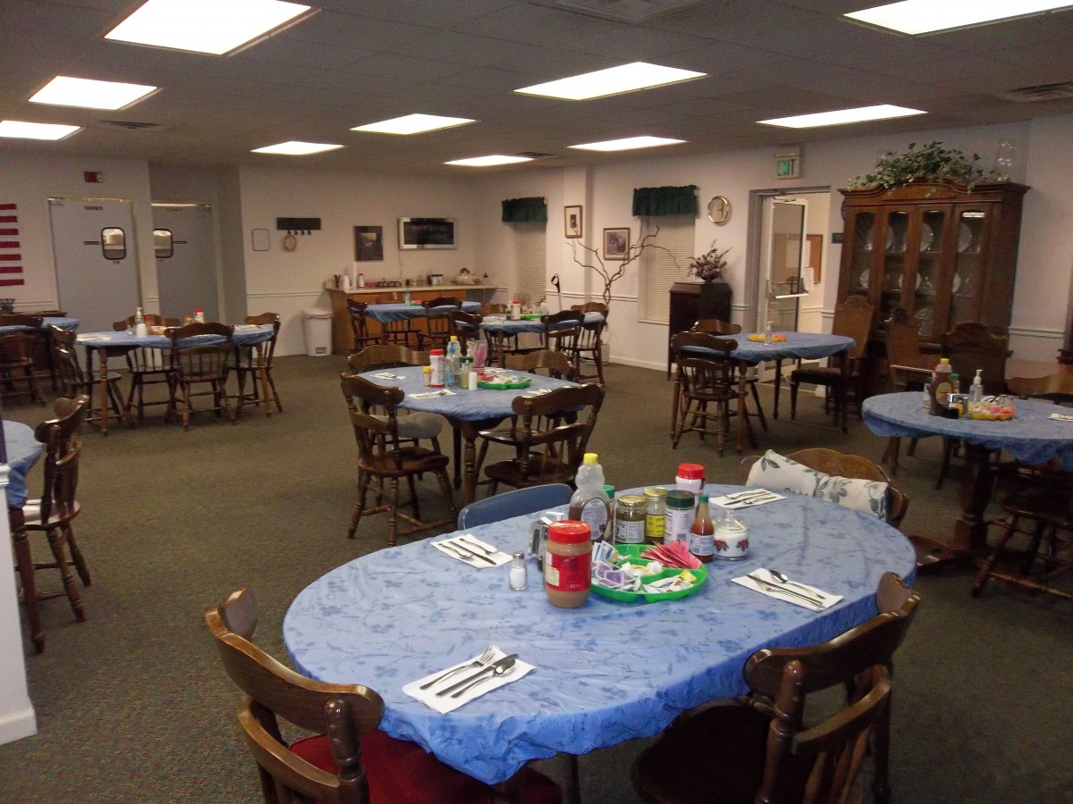 A community dining area with several round tables covered in blue tablecloths, set up for a gathering.