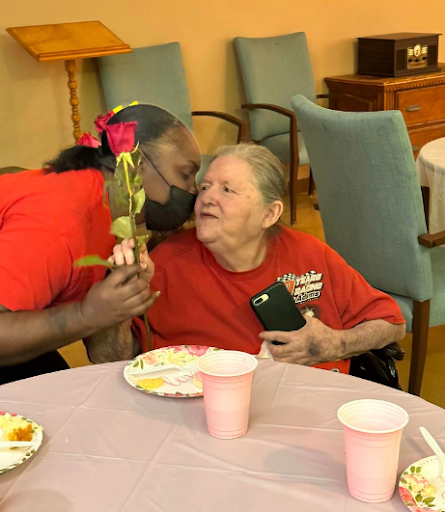 A heartfelt moment between a caregiver and an elderly resident, sharing smiles and a rose.