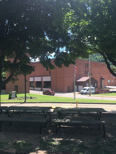 A view of a brick building surrounded by greenery and picnic tables in a park.