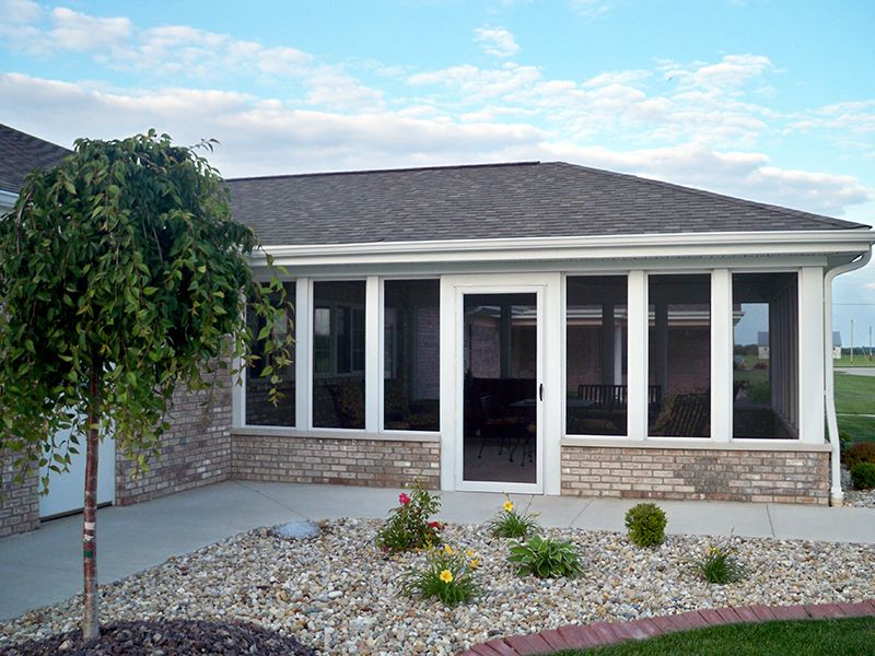 A sunroom with large windows, surrounded by a landscaped garden and patio area.