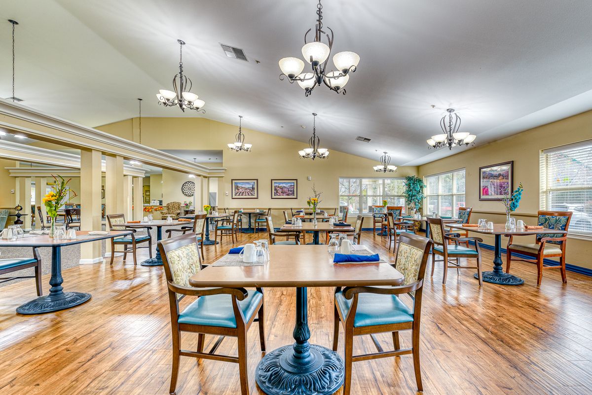A spacious and well-lit dining area with neatly arranged tables and chairs on a wooden floor.