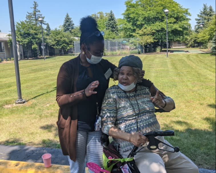 A caregiver and an elderly person enjoying a sunny day in the park.