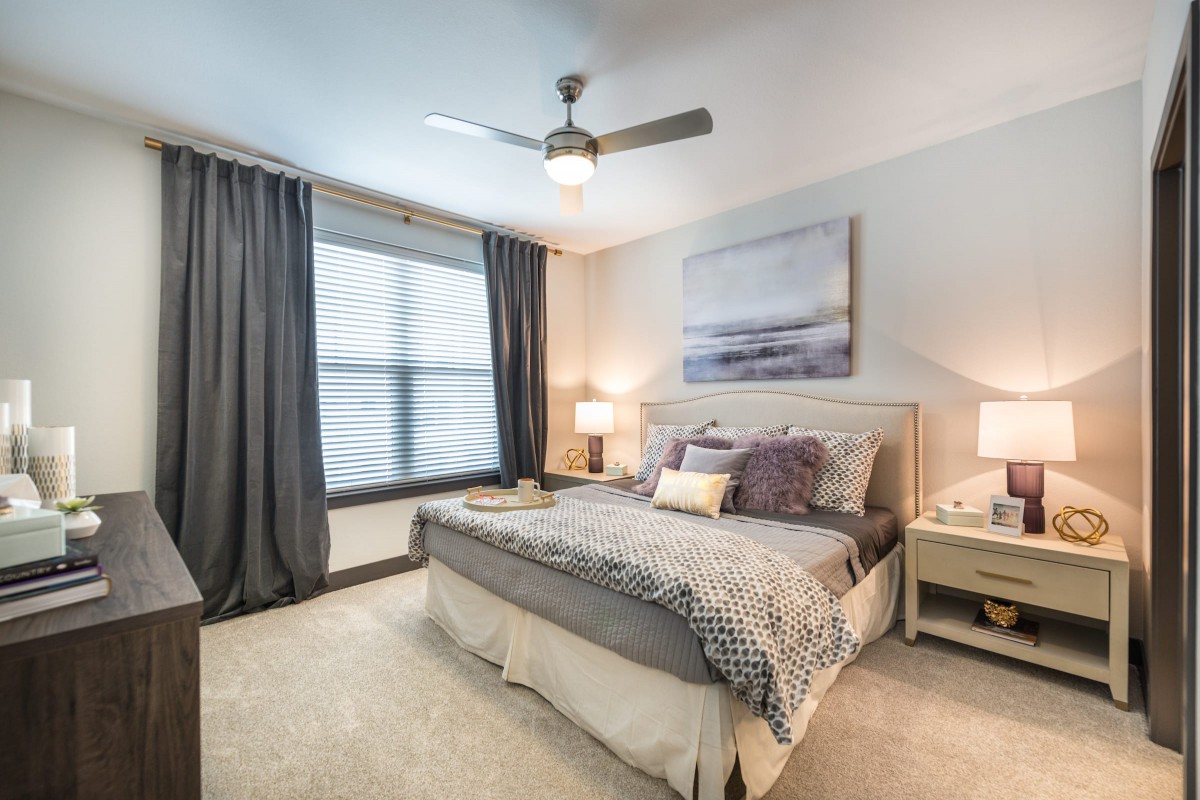 A modern bedroom with stylish decor, featuring a bed, nightstands, and a ceiling fan.