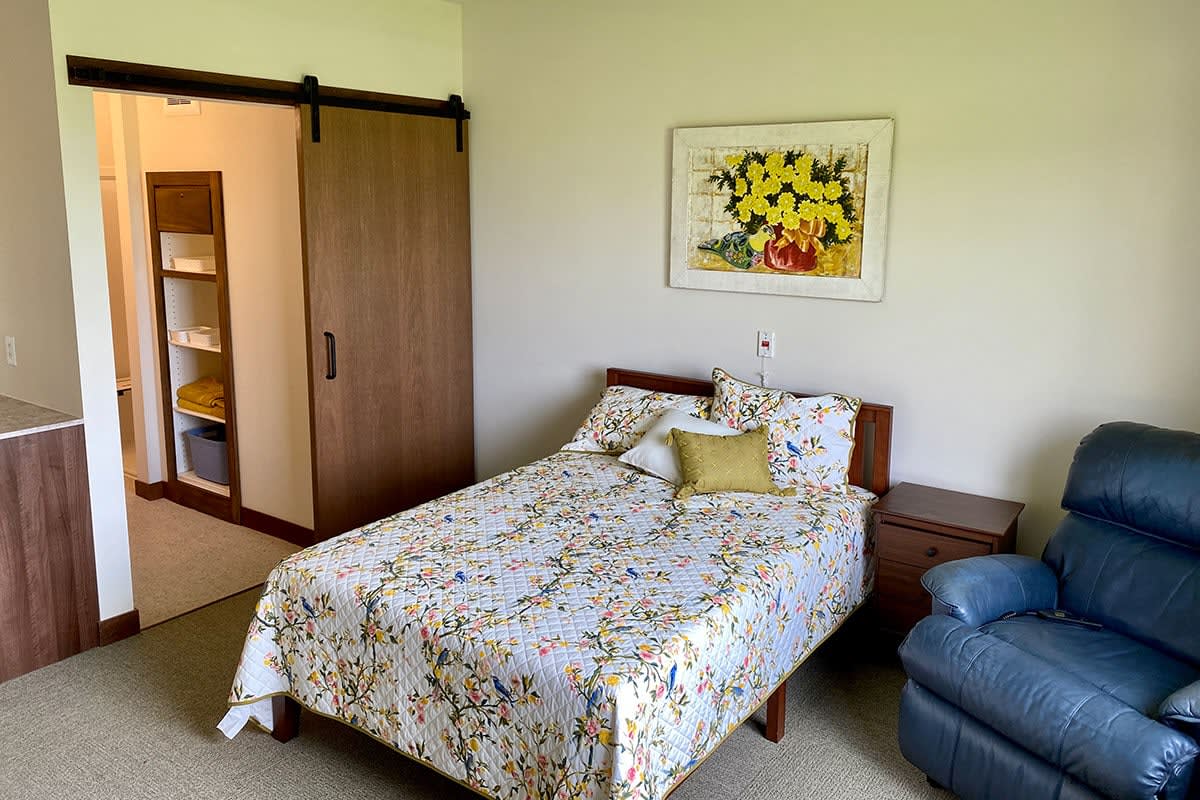 A cozy bedroom featuring a bed with floral bedding, artwork on the wall, and a closet with a sliding door.