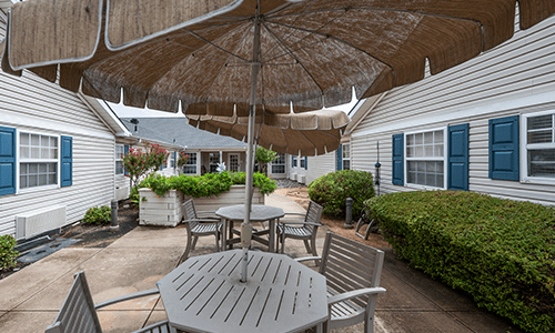 A cozy outdoor patio area featuring tables with umbrellas, surrounded by lush greenery.
