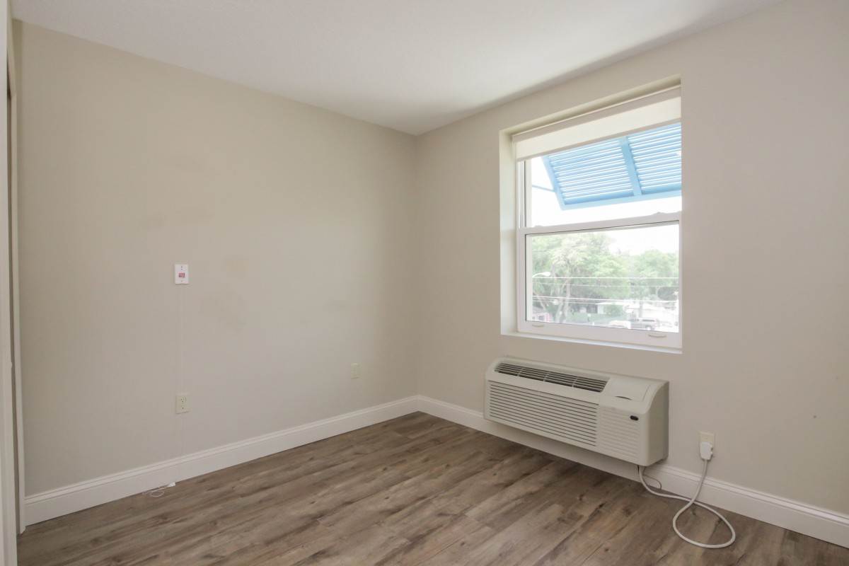 A small empty room with hardwood floors, a window, and an air conditioning unit.
