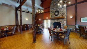 A cozy restaurant interior with a stone fireplace, elegant chandeliers, and wooden flooring.