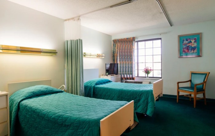 A hospital room with two beds, a television, and a window.
