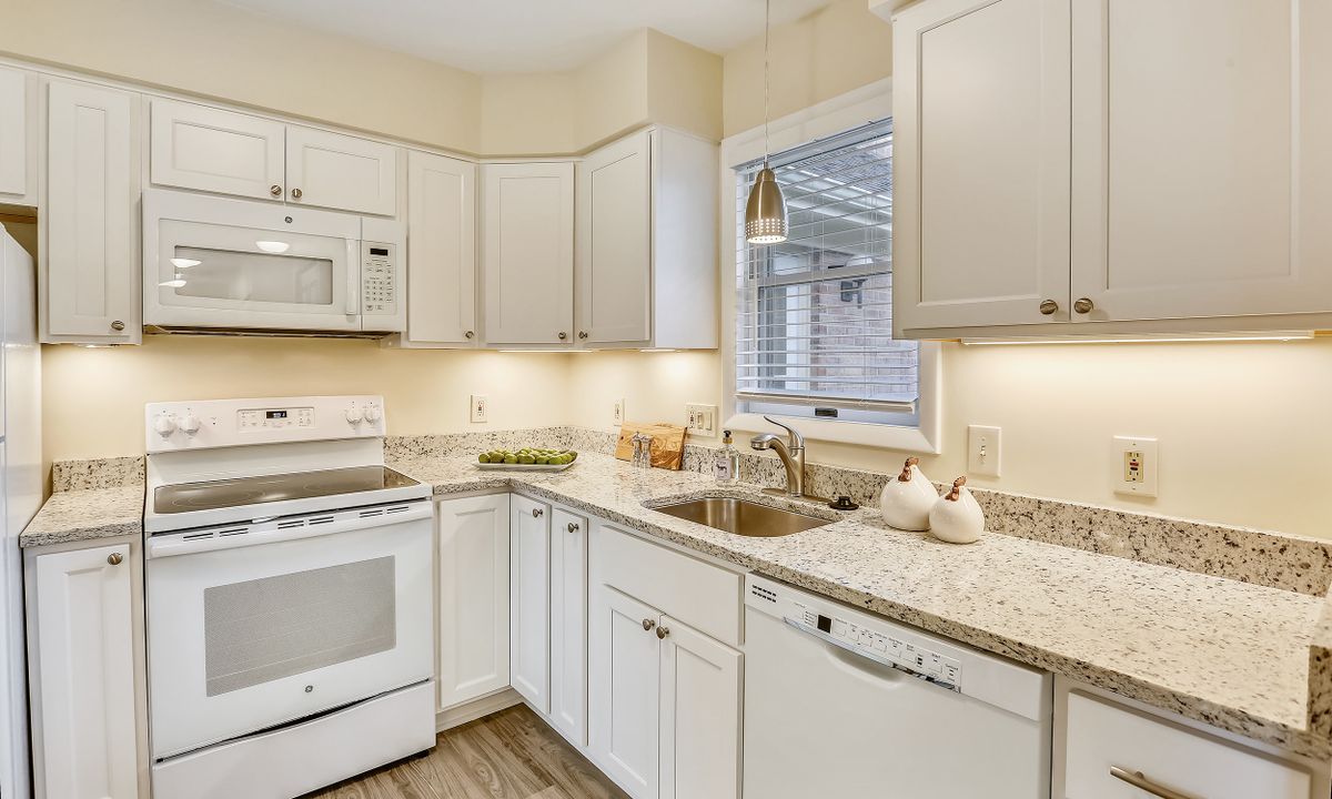 A modern kitchen with white cabinets, appliances, and a window above the sink.