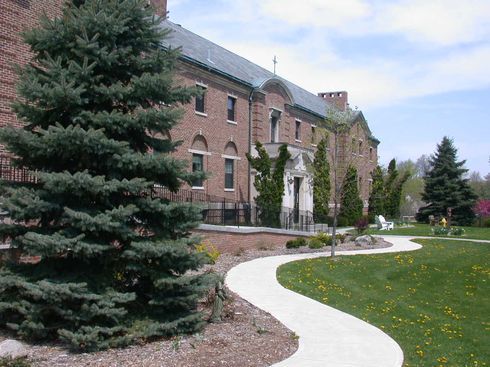 A pathway leads to a large brick building surrounded by trees and greenery.