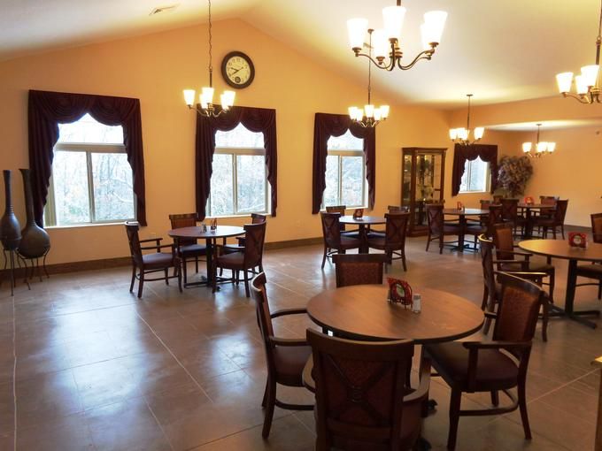 A spacious dining room with several round tables and chairs, elegant chandeliers, and large windows with curtains.