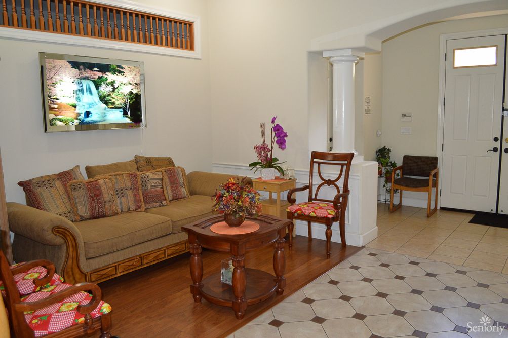 A cozy living room with a comfortable sofa, armchair, and a wooden coffee table. A television is mounted on the wall, and an orchid adds a touch of elegance to the decor.