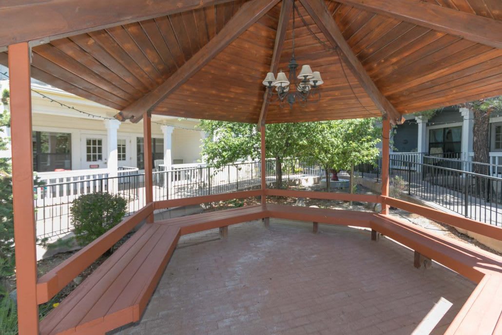 A wooden gazebo with built-in benches, surrounded by a garden setting.
