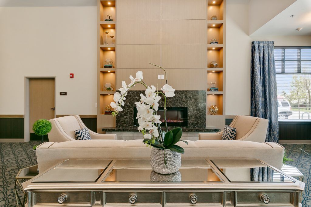 A modern living room featuring a central fireplace, elegant furniture, and a potted orchid on a glass coffee table.