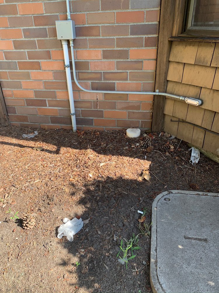 A brick wall with an electrical conduit and scattered debris on the ground.