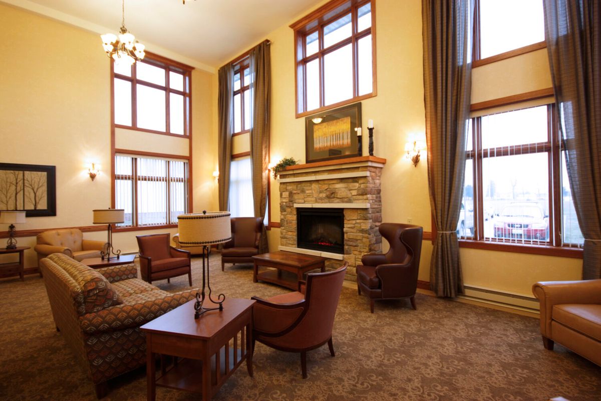 A cozy living room featuring a stone fireplace, surrounded by plush armchairs and large windows with curtains.