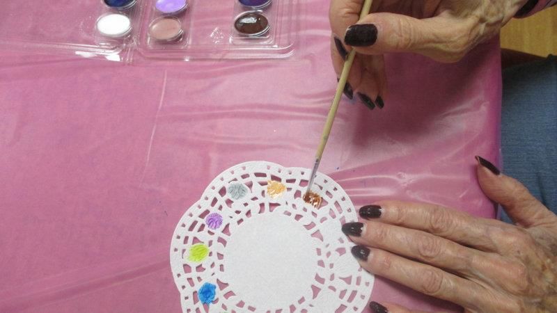 A person painting a decorative doily with watercolors.