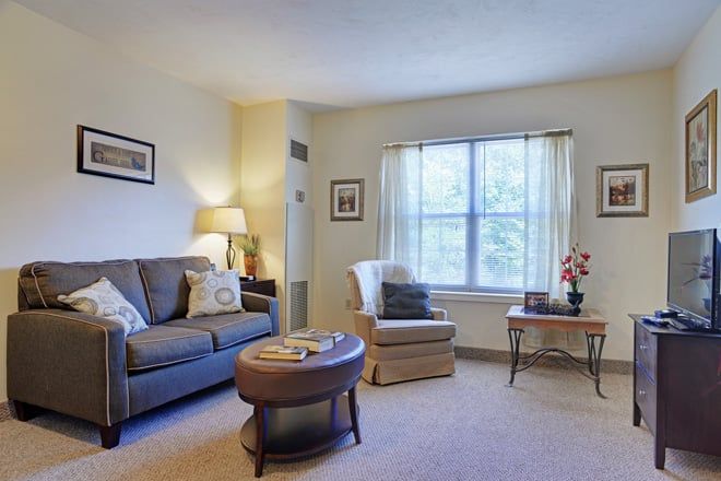 A cozy living room with a sofa, armchair, and coffee table by a window with curtains.