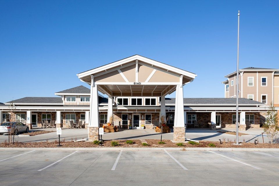 A modern building with a prominent entrance and spacious parking area under a clear blue sky.