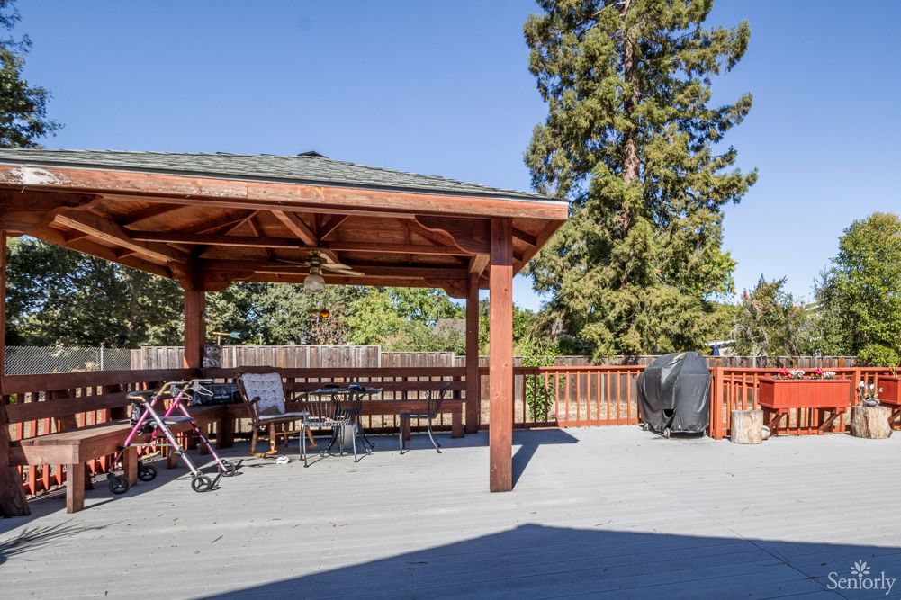 A spacious backyard deck with a wooden pergola, outdoor furniture, and a grill under a clear blue sky.