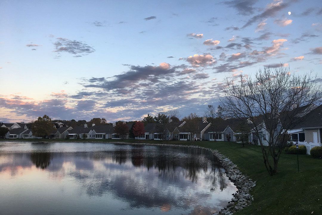 A tranquil lake reflects the evening sky and a row of houses at sunset.