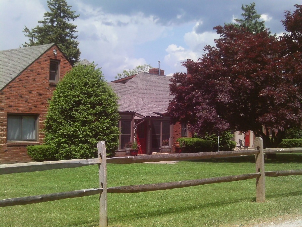 A suburban house with a wooden fence, surrounded by trees and a well-kept yard.