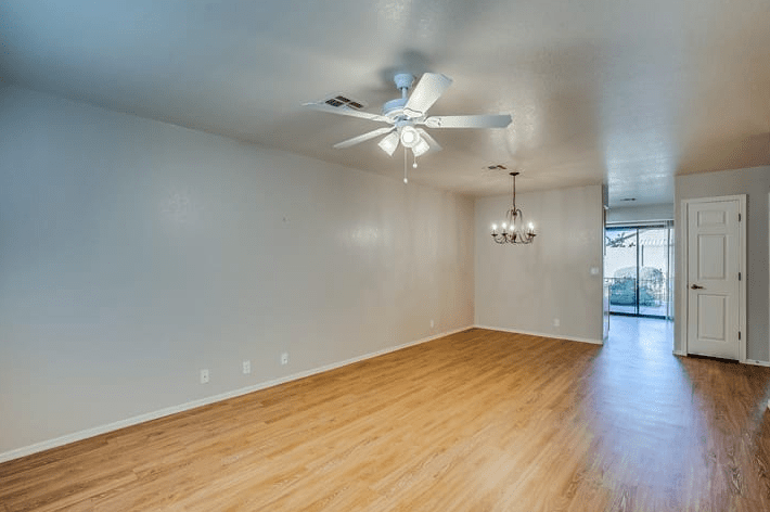 A spacious, empty room with wooden flooring, a ceiling fan, and chandelier lighting.