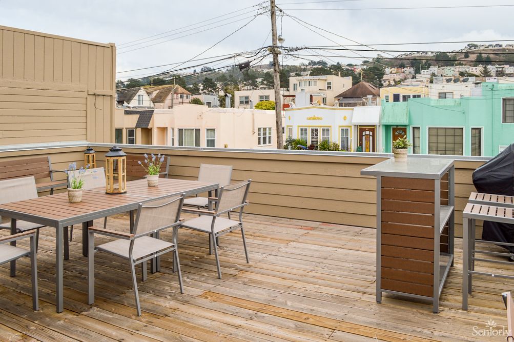 A spacious rooftop deck with a table and chairs, overlooking an urban neighborhood.