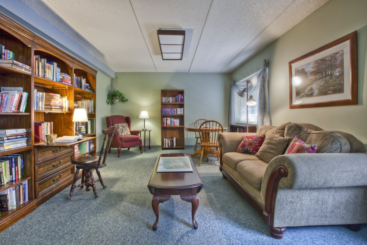 A cozy living room with a sofa, armchair, and bookshelf under warm lighting.