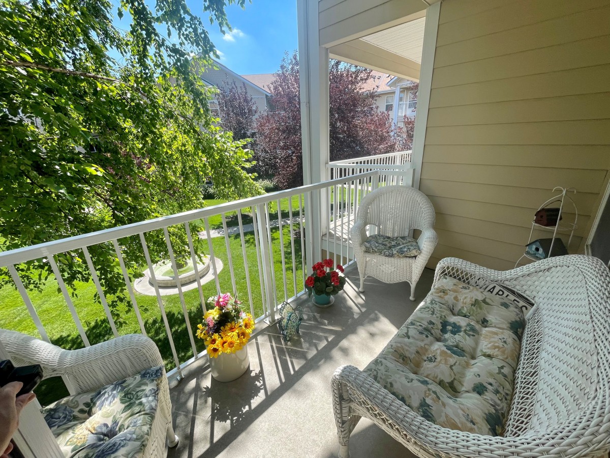 A cozy balcony with wicker furniture and colorful flowers, overlooking a sunny garden.
