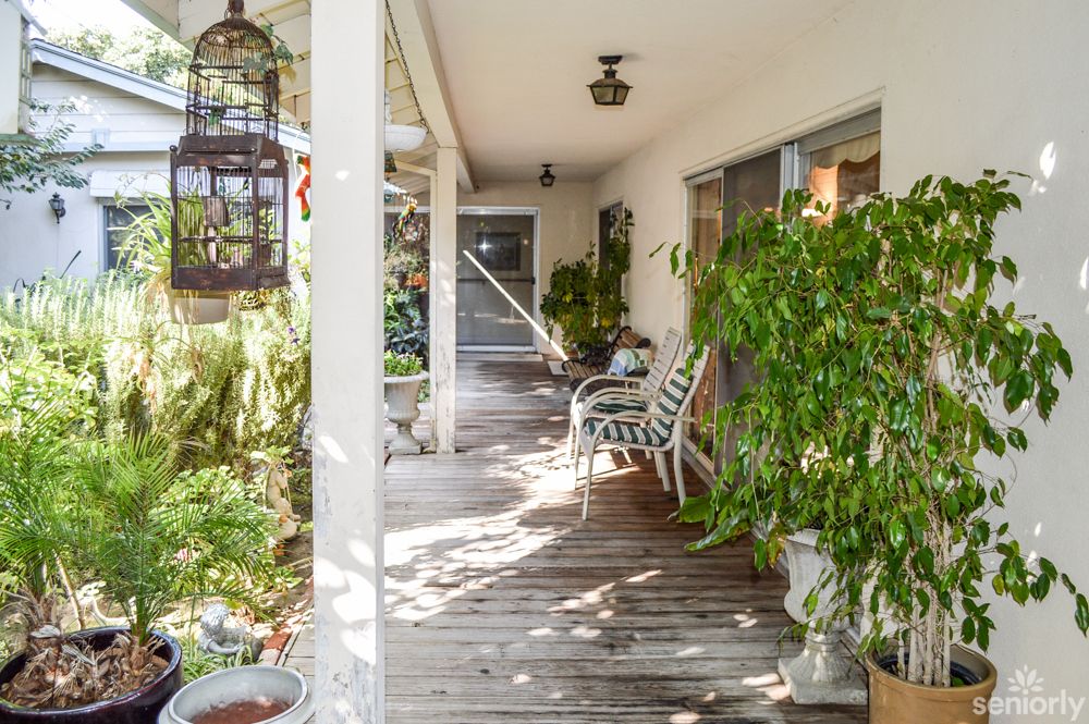 A cozy porch with abundant greenery, featuring wooden flooring and outdoor seating.