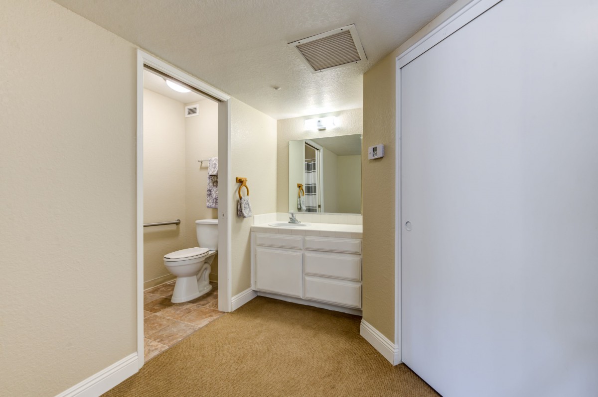A small bathroom with a toilet and vanity sink, featuring a wall mirror and bright lighting.