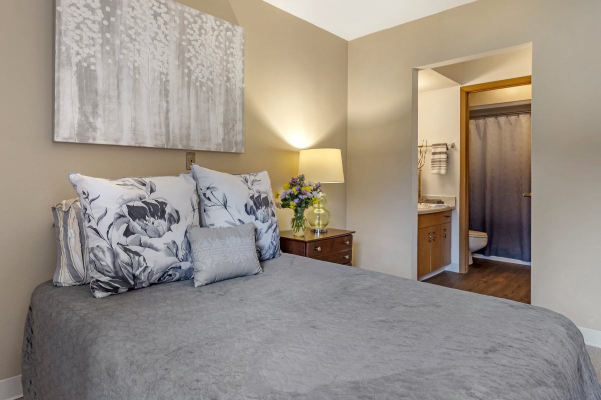 A cozy bedroom with modern decor featuring a bed, nightstand with a lamp, and an adjoining bathroom.
